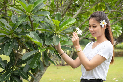 Young woman smiling while standing by tree against plants