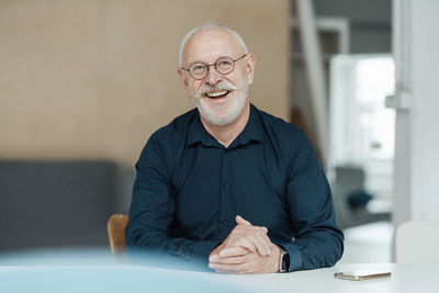 Cheerful businessman sitting with hands clasped at table in office