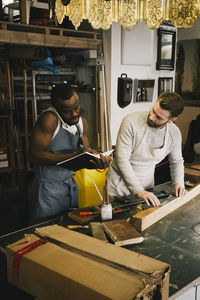 Male entrepreneur taking order through phone while colleague working at upcycling workshop