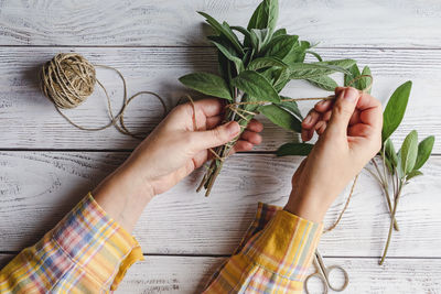 Sage leaf bundle in hands, hemp string and scissors on old wooden table