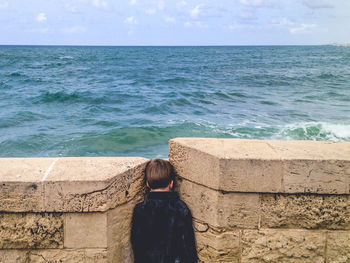 Rear view of boy standing amidst retaining wall against sea