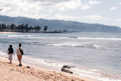 Rear view of people on beach against sky