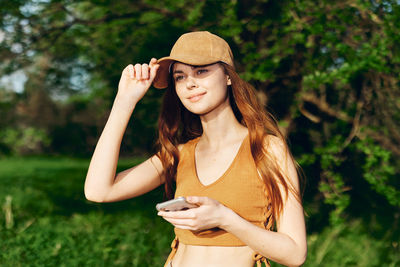 Young woman wearing hat standing against plants