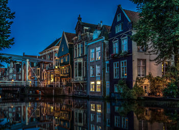 Residential buildings reflecting in canal against clear blue sky at dusk