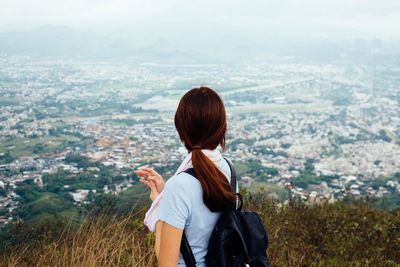 Close-up of woman with backpack standing on hill against cityscape