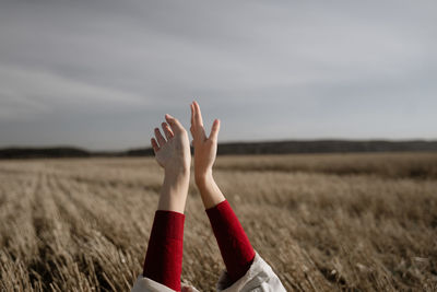 Cropped hand of woman on field against sky