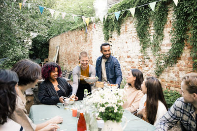 Young woman serving food to male and female friends during social gathering in back yard