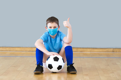 Portrait of boy wearing mask sitting by soccer ball