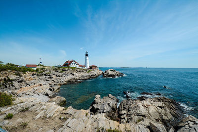 Lighthouse by sea against blue sky