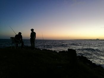 Silhouette people standing on beach against clear sky