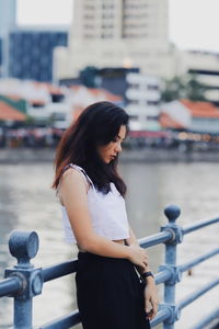 Side view of thoughtful young woman standing on footbridge by river