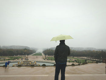 Rear view of man with umbrella walking on wet road during rainy season