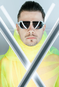 Portrait of man wearing sunglasses holding lighting equipment while standing against wall