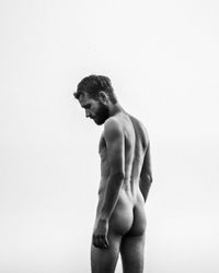 Naked young man standing against white background