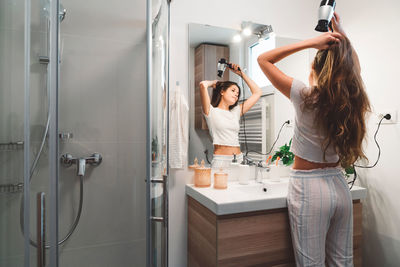 Rear view of young woman using mobile phone while standing in bathroom