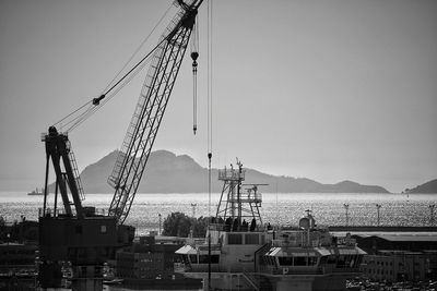 Crane at construction site by sea against clear sky