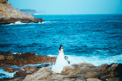 Woman standing on rock by sea against sky