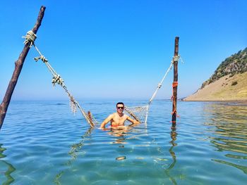 Full length of shirtless man in sea against clear blue sky