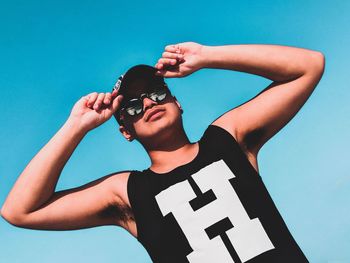 Portrait of young man wearing sunglasses standing against blue wall