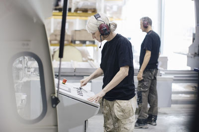 Female worker standing with colleague operating machine at industry