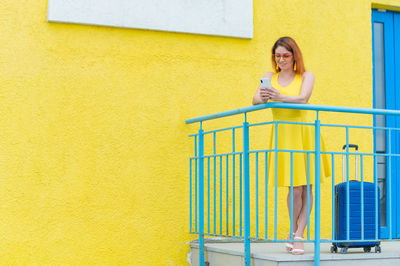 Portrait of a smiling young woman standing against yellow wall