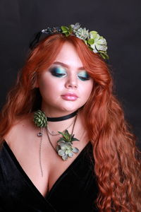 Sensuous young woman wearing wreath and necklace against black background