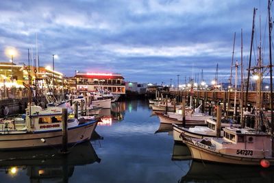 Boats moored in harbor against cloudy sky at dusk