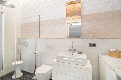 Modern refurbished tiled bathroom with shower zone, toilet, white sink and mirror.