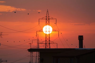 Low angle view of silhouette electricity pylon against sky during sunset