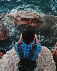 High angle view of young man sitting on cliff over sea