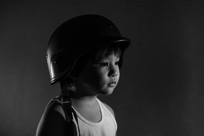 Close-up of cute boy wearing helmet looking away against wall