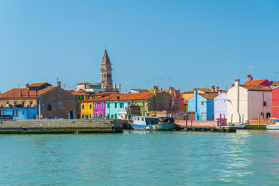 Buildings by river against clear blue sky