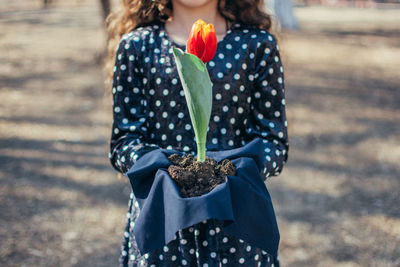 Rear view of woman holding flower standing outdoors