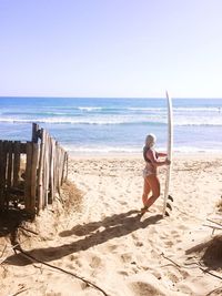 Side view of woman with surfboard at beach against sky