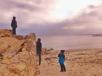 Family enjoying at beach against sky during sunset