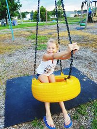 Portrait of smiling girl sitting on swing at park