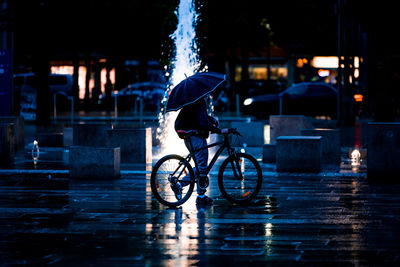 Man riding bicycle on wet street during rainy season at night