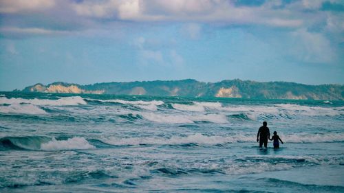 Silhouette father and son in sea against sky