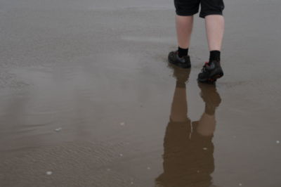 Low section of man standing on beach against sky