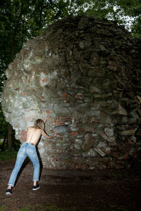 Rear view of shirtless woman pushing rocky structure at park