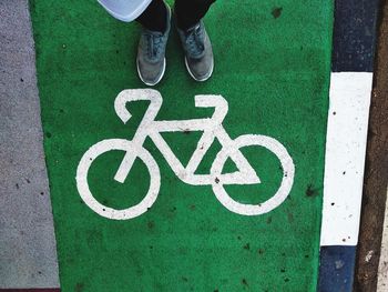 Low section of person standing by bicycle sign on road