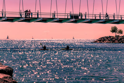 Silhouette people on bridge over sea against sky during sunset