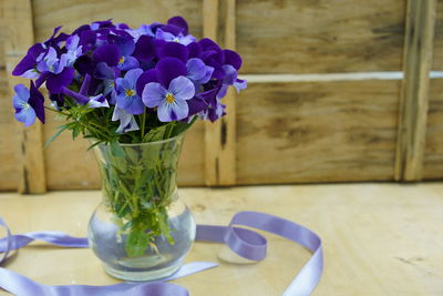 Pansies flower bouquet in clear glass with purple ribbon. wooden background. closeup.