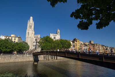 Bridge over river by buildings against blue sky