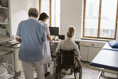 Rear view of disabled patient with female doctor and nurse at medical clinic