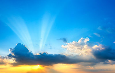 Low angle view of sunlight streaming through clouds