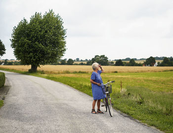 Elderly woman with bicycle by field