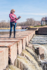 Low angle view of an adult woman standing on a brick walkway in the park holding a gimbal with phone 