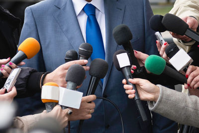 Cropped hands of journalists holding microphones in front of businessman