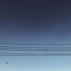 Low angle view of power lines against clear blue sky